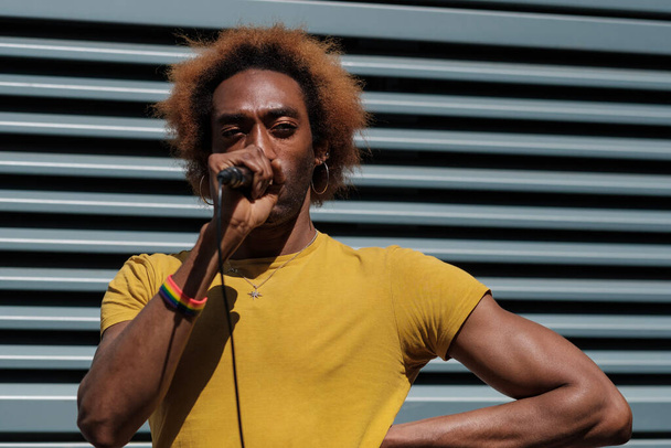 Niebinarny młody piosenkarz występujący na londyńskiej ulicy. Trzyma mikrofon i nosi żółtą koszulkę. Kręcone blond włosy. - Zdjęcie, obraz