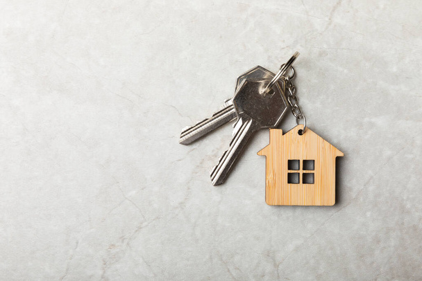Hausschlüssel mit Schlüsselanhänger in der Form eines Haus.Komposition auf grauem Marmorhintergrund.Designelement.Immobilien- und Versicherungskonzept.Platz zum Kopieren. - Foto, Bild