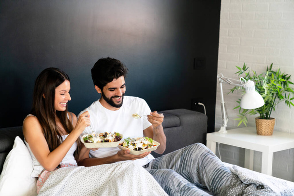Healthy breakfast in bed. Young beautiful love couple is sitting in bed and having breakfast. - Valokuva, kuva