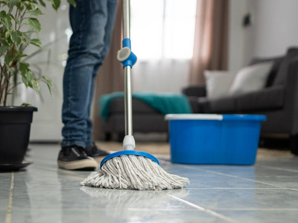 Close up de pernas de homem limpando o chão da sala de estar com uma esfregona - Foto, Imagem