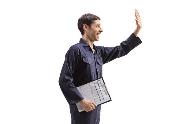 Worker in a niform holding a clipboard and waving isolated on white background - Zdjęcie, obraz