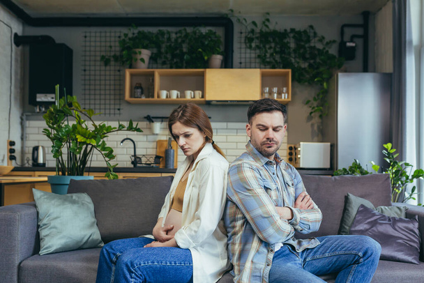 Family conflict. Young couple, pregnant woman and man sitting on sofa at home with their backs to each other. Do not talk, offended. - Valokuva, kuva