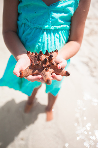 Маленька чарівна дівчинка з зіркою в руках на тропічному пляжі
 - Фото, зображення