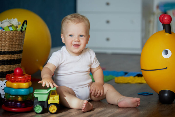 Cute baby boy playing with toys while sitting on the floor at home. Early development of children. happy childhood. Advertisement for children's products - 写真・画像