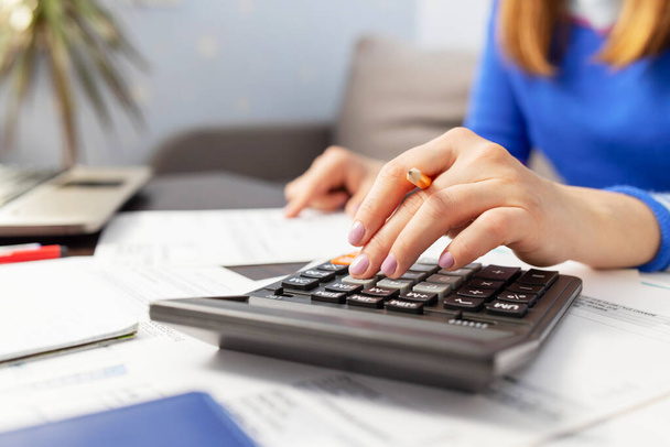 Vrouw met behulp van rekenmachine voor het berekenen van binnenlandse rekeningen thuis, het doen van papierwerk voor het betalen van belastingen - Foto, afbeelding