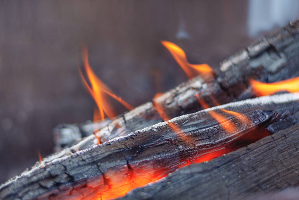 Defokussiertes Feuerholz brennt im Kamin in den Flammen eines warmroten Feuers auf dunklem Hintergrund. Briketts glühen und brennen aus nächster Nähe - Foto, Bild