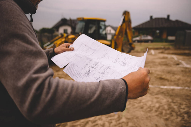 Architect showing house build plans at the building site. Engineer working with blueprints outside on construction site - Φωτογραφία, εικόνα
