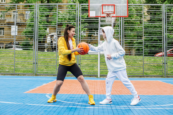 女の子と彼女の弟,ティーンエイジャー,オープン空の下で近代的なバスケットボールコートでバスケットボールをプレイ.スポーツ、趣味、健康的なライフスタイルの概念. - 写真・画像