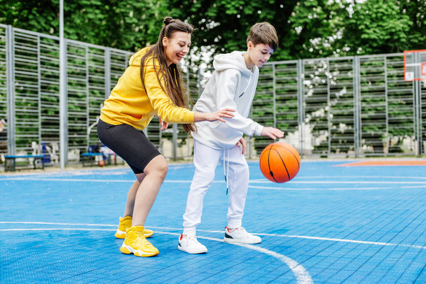 Mädchen und ihr jüngerer Bruder, Teenager, spielen Basketball auf einem modernen Basketballfeld unter freiem Himmel. Konzept von Sport, Hobbys und gesundem Lebensstil. - Foto, Bild