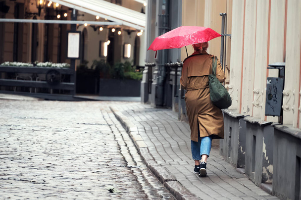 Una donna cammina lungo una strada bagnata e tiene un ombrello in caso di pioggia. Brutto tempo in città. - Foto, immagini
