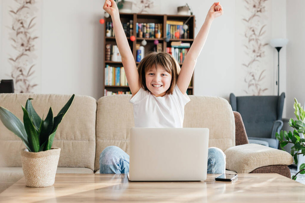 Meisje schoolmeisje thuis voor een laptop is blij met succes. Online leren, afstandsonderwijs en -cursussen. - Foto, afbeelding