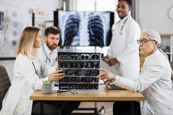 Qualified international doctors of differents ages gathering at boardroom for examining x ray scan of lungs and brain. Medical specialists thinking about diagnosis and treatment of severe patient. - Foto, immagini