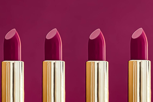 Purple lipsticks in golden tubes on colour background, luxury make-up and cosmetics for beauty brand product design concept - Фото, зображення