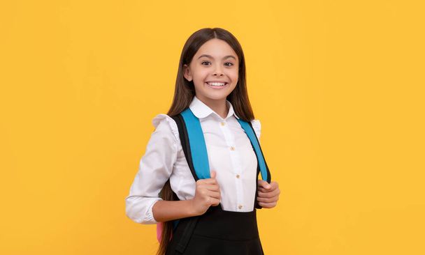 Nettes Kind mit Schultasche. glücklich Teenager Mädchen tragen Rucksack. zurück zur Schule. Wissenstag. Konzept der Bildung. Kind mit langen Haaren in Uniform auf gelbem Hintergrund. 1. glückliche Kindheit. - Foto, Bild