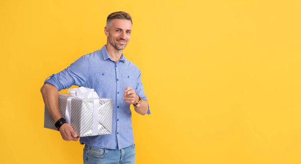 happy mature man hold box pointing finger on yellow background, copy space, shopping. - Zdjęcie, obraz