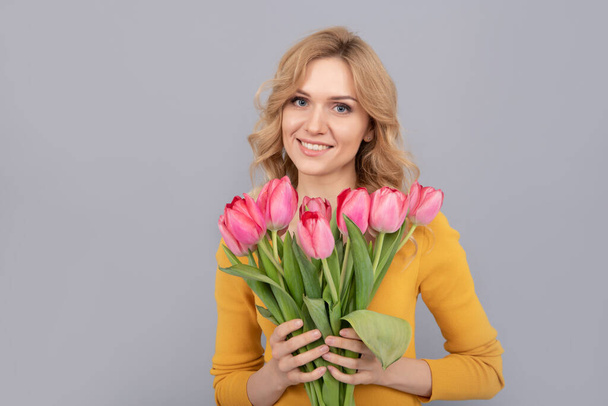 happy woman with tulips. lady hold flowers for spring holiday. girl with bouquet on grey background. floral present for womens day. 8 march and mothers day. - Fotó, kép