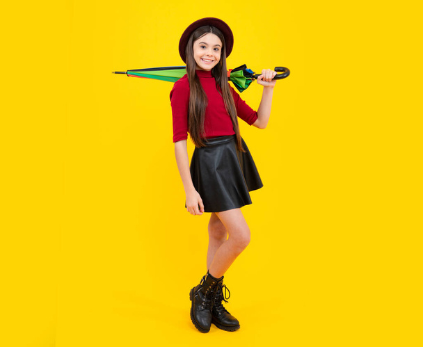 Teen Mädchen mit Regenschirm im Herbstwetter isoliert auf gelbem Hintergrund. Herbstliche Kinderkleidung. Glückliches Teenager-Porträt. Lächelndes Mädchen - Foto, Bild