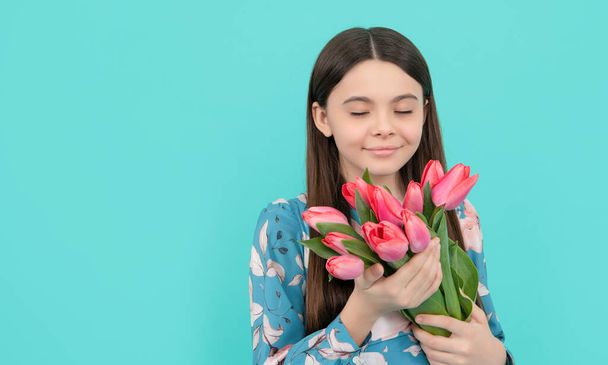 kid hold flowers for 8 of march. teen girl with spring bouquet on blue background. floral present. copy space. happy child smell tulips. mothers or womens day. - Photo, Image