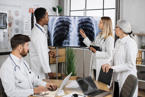International team of doctors gathering together for discussing lungs x ray result in progressive diagnostic centre. Multiethnic qualified staff having work meeting for searching ways of treatment. - Foto, Imagem