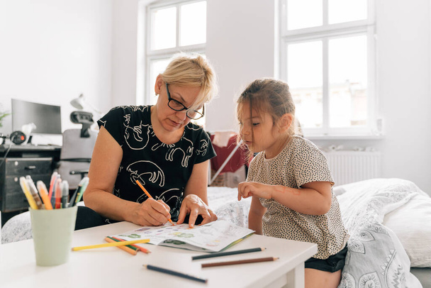 Mature woman granny with grandchild preschool girl drawing together at home. . High quality photo - Foto, Imagem