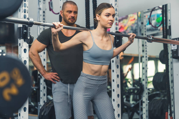 Proud confident caucasian young adult fit woman at gym weightlifting supported by her personal trainer. Sports concept. High quality photo - Photo, Image