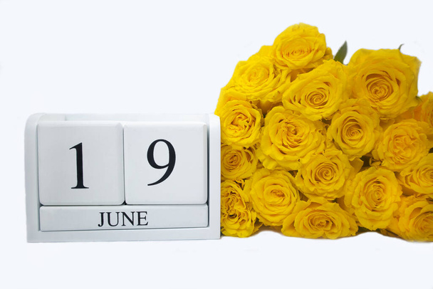 Wooden, white calendar June 19, bouquet of yellow roses lie next to it . The concept of holidays, important date, event . High quality photo - Photo, Image