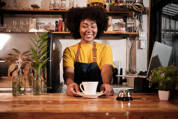 Afro-Amerikaanse vrouwelijke barista biedt kopje koffie aan de klant met een vrolijke glimlach, happy service werkt in casual restaurant cafe, jonge kleine bedrijven startup ondernemer. - Foto, afbeelding