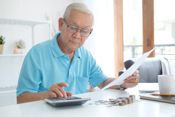 Starší muž počítá finance. Vážný muž sedící u stolu poblíž účtu za elektřinu a počítající výdaje. - Fotografie, Obrázek