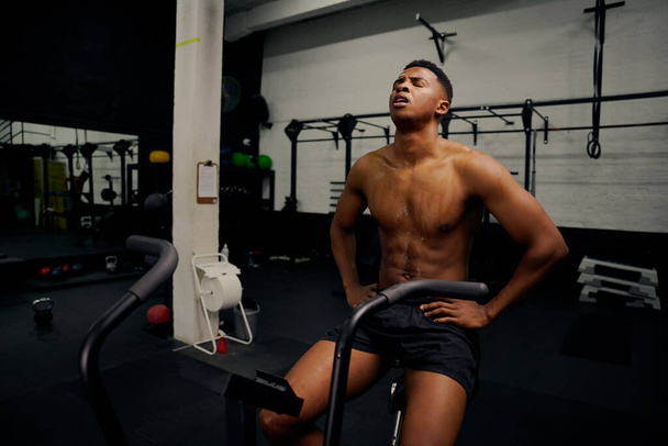 African American male using an elliptical trainer during cross fit training. Male personal trainer exercising intensely in the gym. High quality photo - Photo, Image