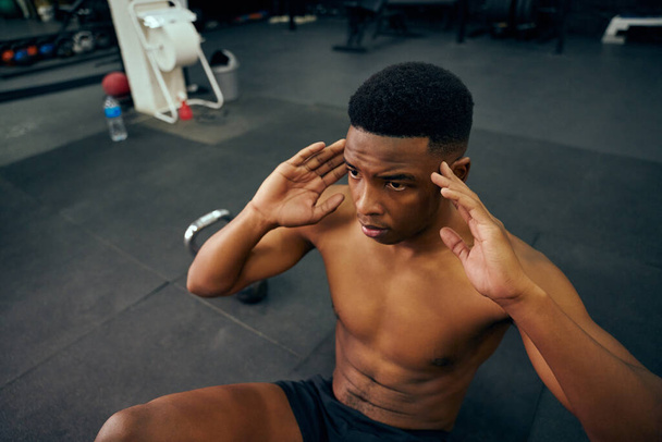 Young, topless African American male doing push-ups on the floor in the gym. Mixed race male personal trainer exercising doing cross fit indoors. High quality photo - Фото, изображение