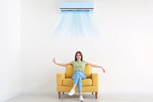 Young woman sitting in armchair near blowing air conditioner at home - Photo, image