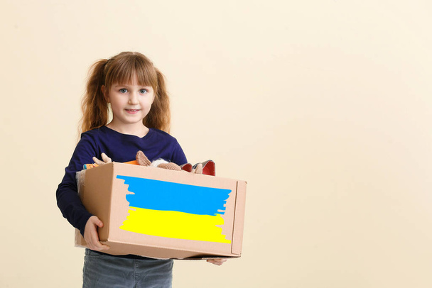 Little girl with humanitarian aid for Ukraine on light background - Photo, Image