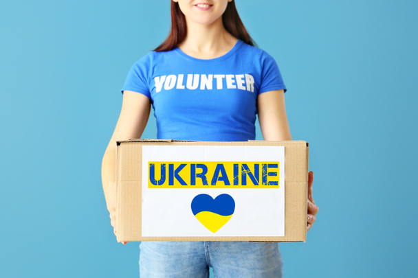 Vrouwelijke vrijwilliger met donatie doos op blauwe achtergrond. Humanitaire hulp aan Oekraïne - Foto, afbeelding