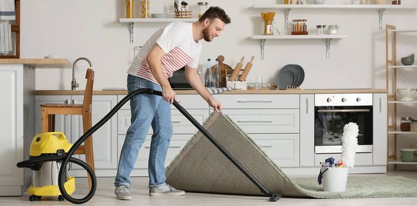 Young man vacuuming floor in kitchen - Φωτογραφία, εικόνα