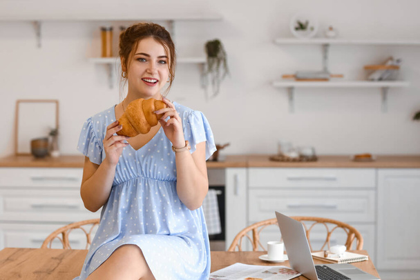 Hermosa mujer joven comiendo croissant en la cocina - Foto, Imagen