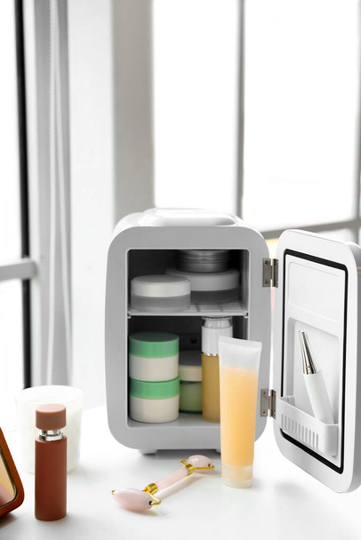 Masada kozmetik ürünleri olan küçük bir buzdolabı aç - Fotoğraf, Görsel