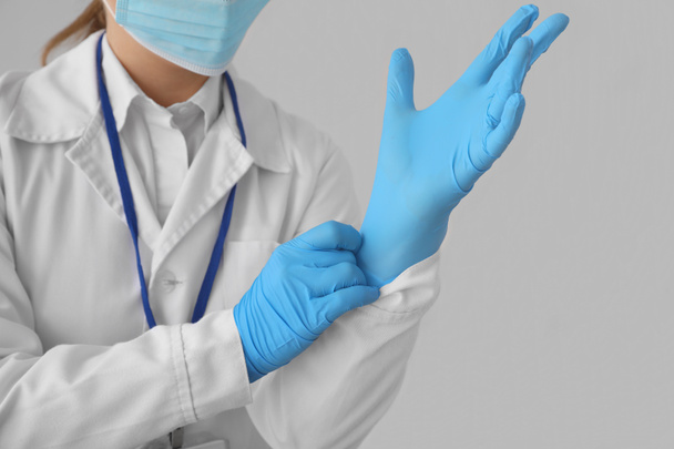 Femme médecin portant des gants en caoutchouc sur fond gris - Photo, image