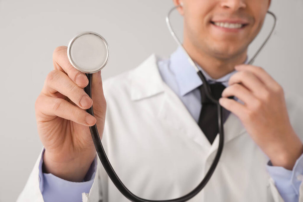 Young male doctor with stethoscope on grey background, closeup - Zdjęcie, obraz