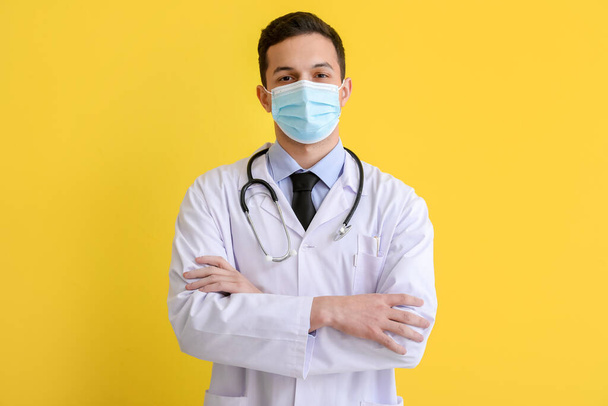 Man arts in medisch masker op gele achtergrond - Foto, afbeelding