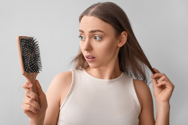 Mujer joven con problemas de pérdida de cabello sosteniendo cepillo sobre fondo claro - Foto, Imagen