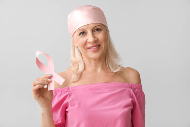 Ältere Frau mit rosa Schleife auf hellem Hintergrund. Brustkrebs-Aufklärungskonzept - Foto, Bild