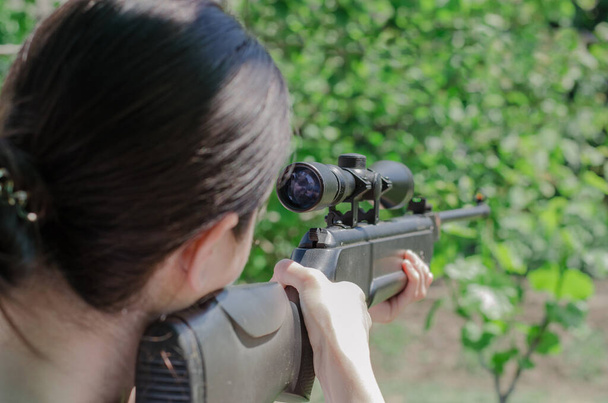 Снайперская девушка держит в руках пистолет. Охотник смотрит в оптический прицел сзади. Глядя в поле зрения снайперской винтовки - Фото, изображение