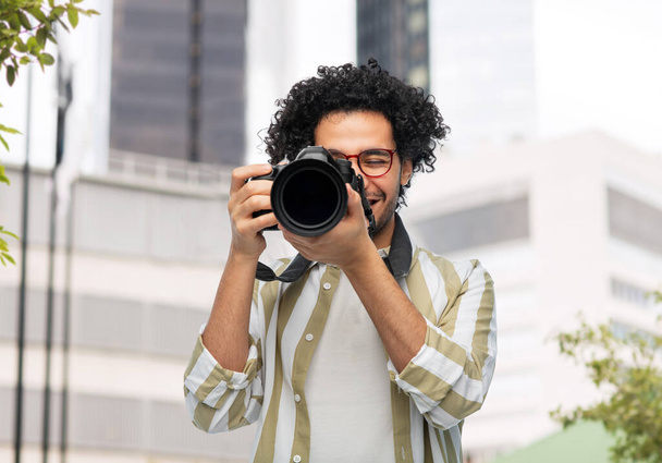 photography, profession and people and concept - happy smiling man or photographer in glasses with digital camera over city background - Фото, изображение