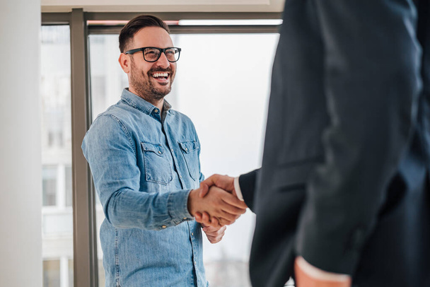 Happy business partners shaking hands in meeting. Entrepreneurs congratulating over successful deal. They are standing in corporate office. - Photo, Image