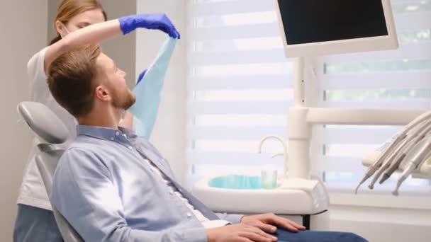 Молодий європейець у стоматологічному кріслі посміхається лікарю. Вичищаю зуби з карієсу. Поняття безболісного лікування зубів - Кадри, відео
