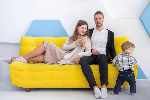 Studioaufnahme einer dreiköpfigen jungen Familie auf einem gelben Sofa. - Foto, Bild