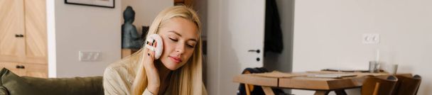 Blondi nuori nainen tekee meikkiä istuessaan sohvalla kotona - Valokuva, kuva