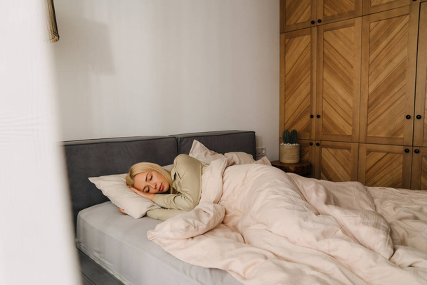 Joven mujer rubia durmiendo tumbada en la cama en casa - Foto, imagen