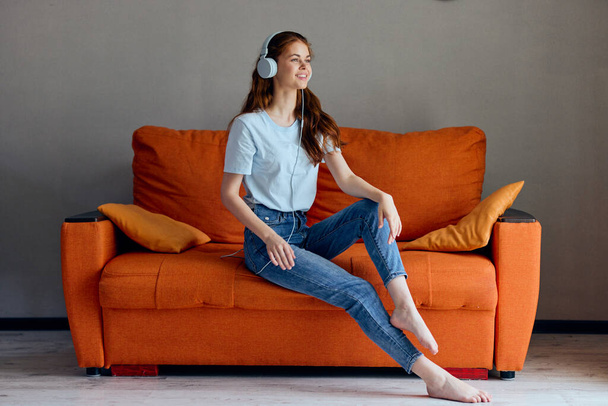 hermosa mujer escuchando música con auriculares en el sofá naranja inalterado. Foto de alta calidad - Foto, imagen