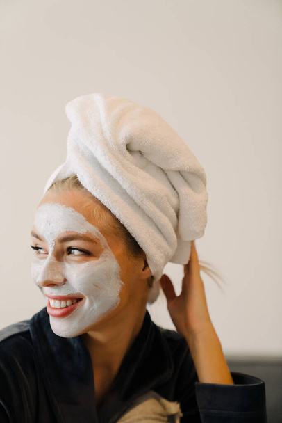 Young woman with face mask laughing while sitting in bed at home - Foto, Imagem